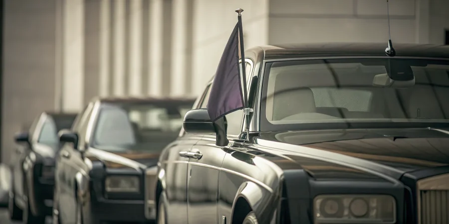 A funeral lead car with a purple flag guides a procession of vehicles.