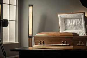 A classic wood casket with a soft white interior in a studio setting.