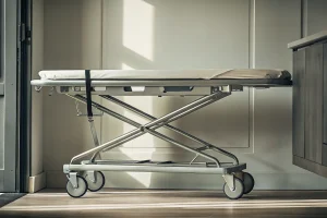 A mortuary hydraulic body lift with adjustable straps and locking wheels for safe body transport.